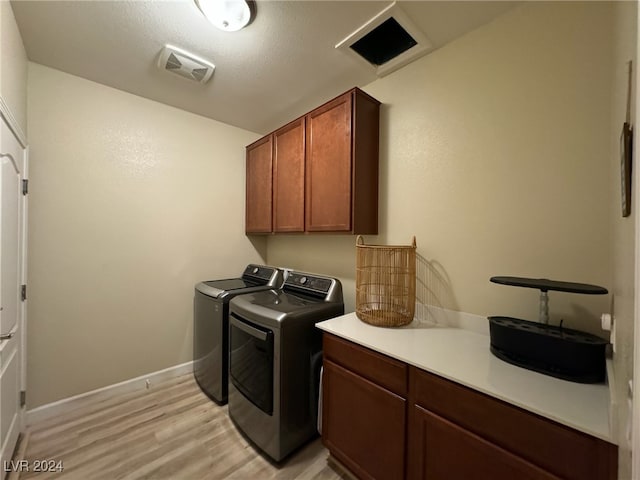 laundry area with a textured ceiling, separate washer and dryer, light hardwood / wood-style flooring, and cabinets