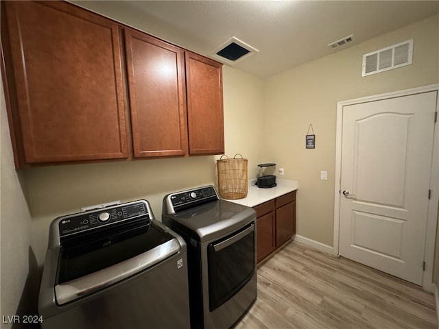 clothes washing area with cabinets, light wood-type flooring, and washer and dryer