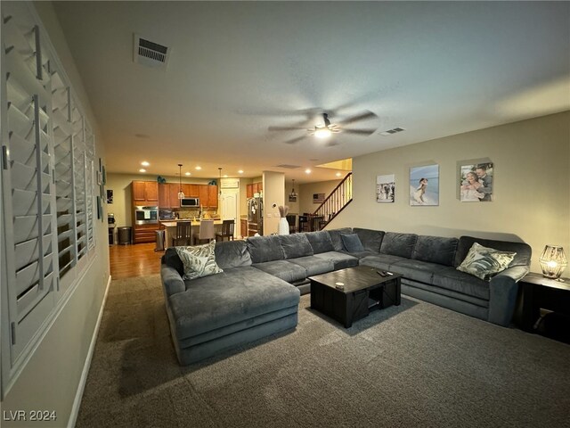 living room with a large fireplace, dark colored carpet, and ceiling fan