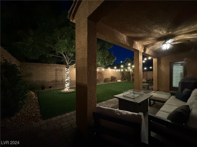 patio at twilight with ceiling fan, a yard, and an outdoor fire pit