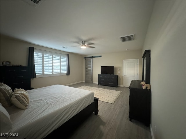 bedroom featuring wood-type flooring, ceiling fan, and a barn door