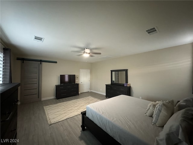 bedroom with wood-type flooring, ceiling fan, and a barn door