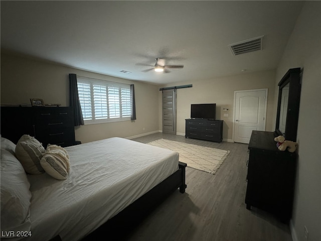 bedroom with a barn door, wood-type flooring, and ceiling fan