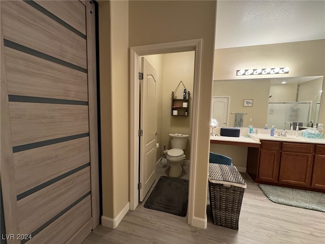 bathroom with wood-type flooring, a shower with door, vanity, and toilet