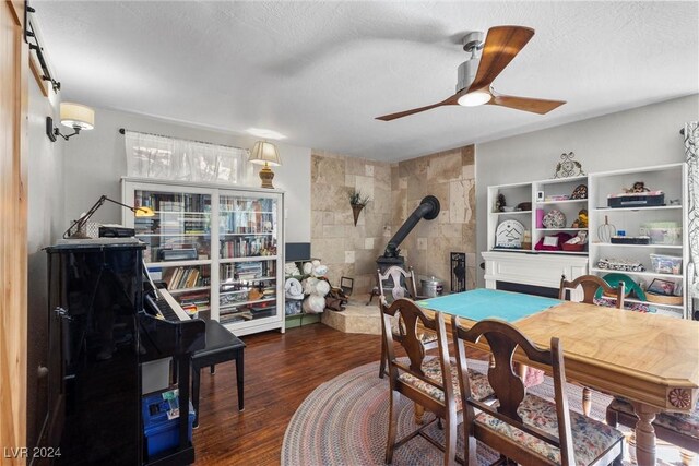 dining area with a wood stove, ceiling fan, dark wood-type flooring, a textured ceiling, and tile walls