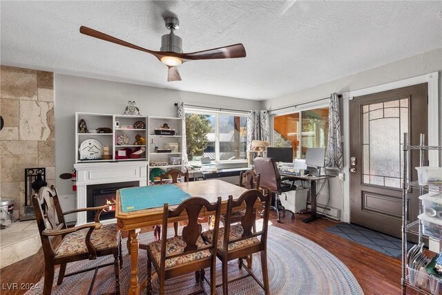 dining space featuring hardwood / wood-style floors, a baseboard heating unit, ceiling fan, a fireplace, and a textured ceiling