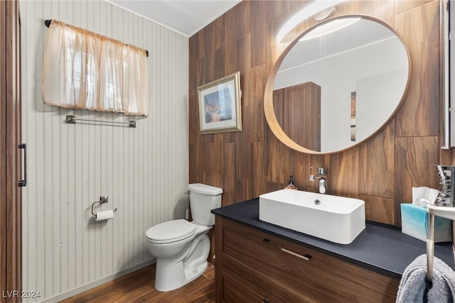 bathroom with wood-type flooring, vanity, toilet, and wood walls