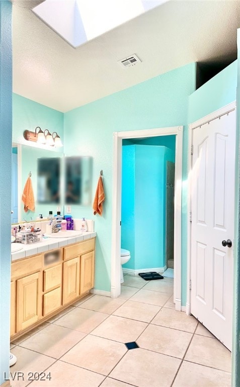 bathroom with a skylight, vanity, tile patterned flooring, and toilet