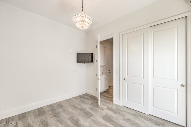 unfurnished bedroom with an inviting chandelier, light wood-type flooring, and a closet