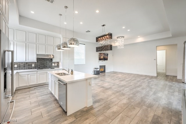 kitchen with appliances with stainless steel finishes, hanging light fixtures, light hardwood / wood-style floors, white cabinetry, and an island with sink