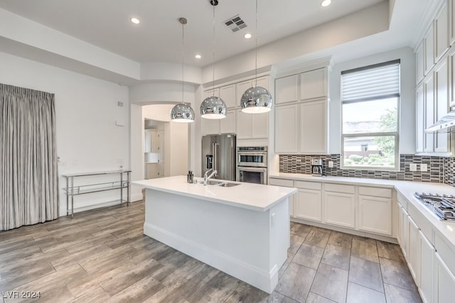 kitchen with decorative light fixtures, a center island with sink, white cabinetry, stainless steel appliances, and light hardwood / wood-style floors