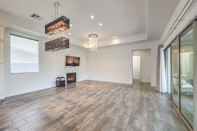 unfurnished living room with an inviting chandelier, light hardwood / wood-style flooring, and a raised ceiling