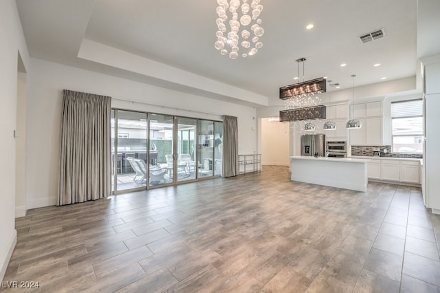 unfurnished living room featuring an inviting chandelier and light hardwood / wood-style flooring