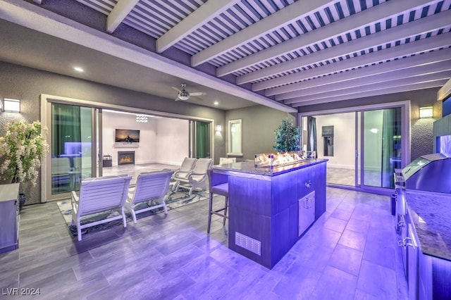 kitchen featuring ceiling fan, beamed ceiling, hardwood / wood-style flooring, a center island, and a breakfast bar area