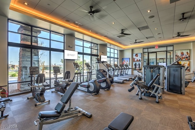 gym with a drop ceiling, a high ceiling, a tray ceiling, and ceiling fan