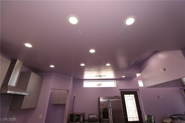 interior space with white cabinetry, stainless steel fridge with ice dispenser, and wall chimney exhaust hood