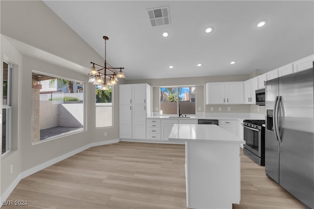 kitchen with appliances with stainless steel finishes, lofted ceiling, decorative light fixtures, white cabinets, and light hardwood / wood-style flooring