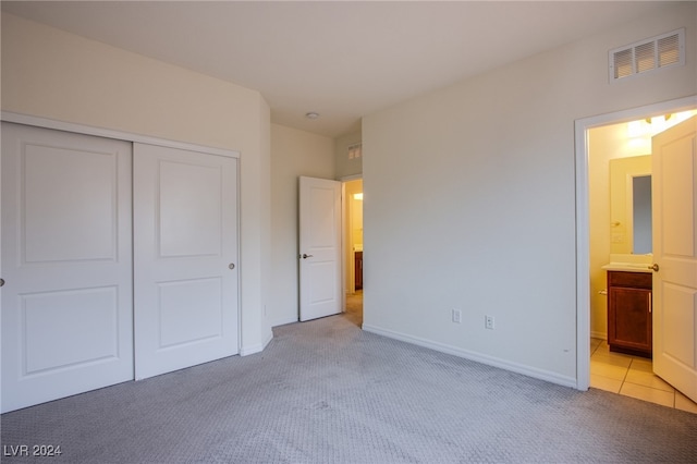 unfurnished bedroom with light carpet, ensuite bathroom, and a closet