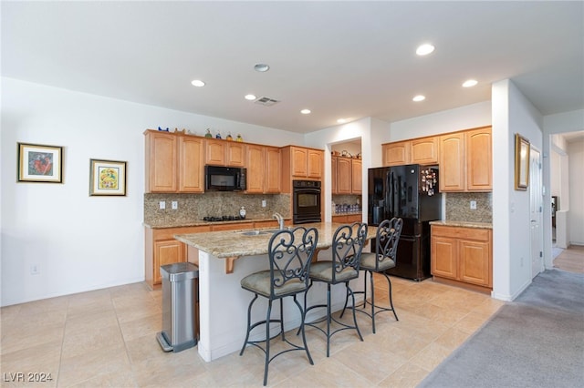 kitchen with decorative backsplash, an island with sink, black appliances, and a kitchen breakfast bar