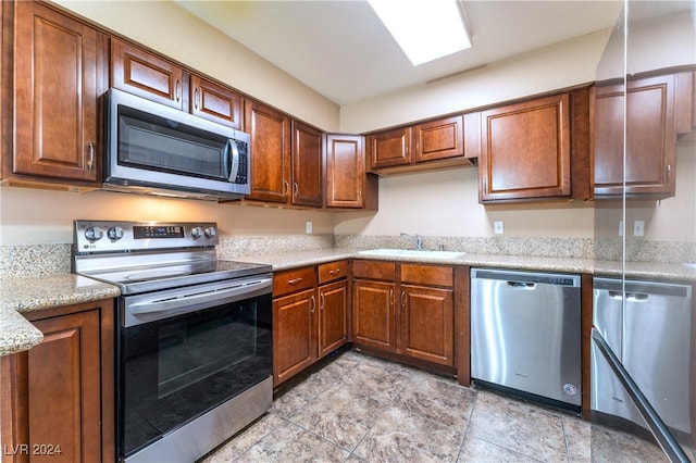 kitchen with stainless steel appliances, light stone counters, and sink