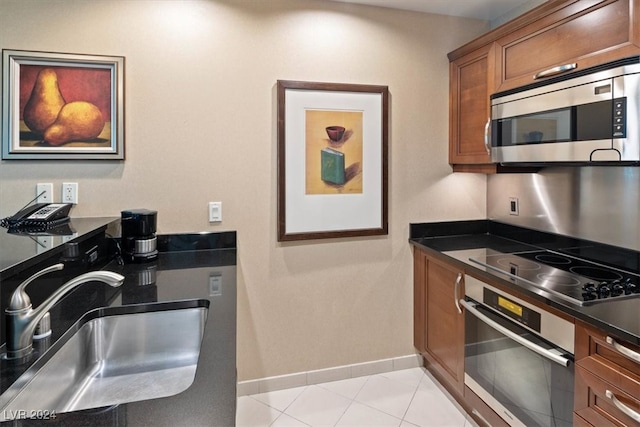 kitchen with dark stone countertops, light tile patterned flooring, appliances with stainless steel finishes, and sink