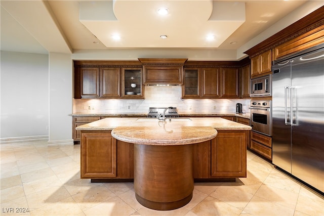 kitchen featuring light stone countertops, a kitchen island with sink, and built in appliances