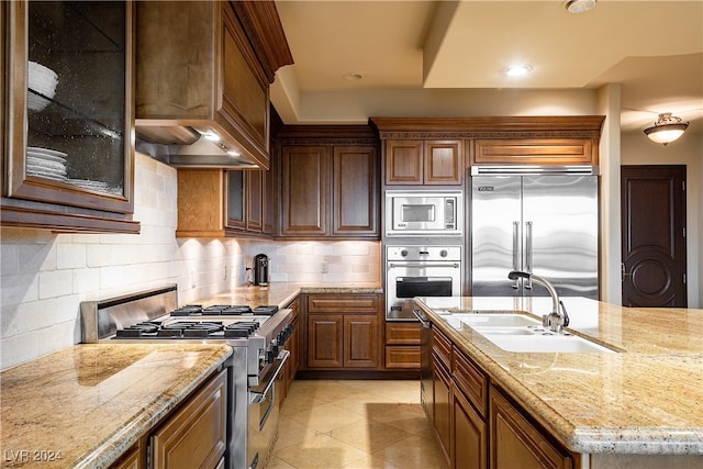 kitchen with light stone counters, light tile patterned flooring, sink, tasteful backsplash, and built in appliances