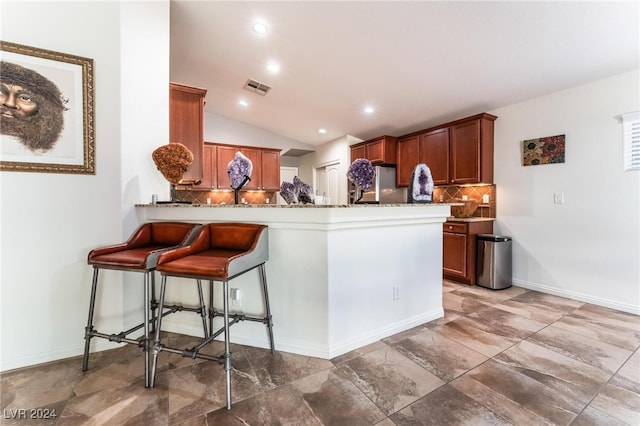 kitchen featuring kitchen peninsula, backsplash, stainless steel refrigerator, a breakfast bar, and vaulted ceiling