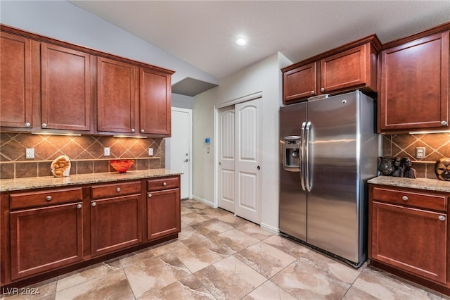 kitchen featuring light stone countertops, vaulted ceiling, and stainless steel fridge