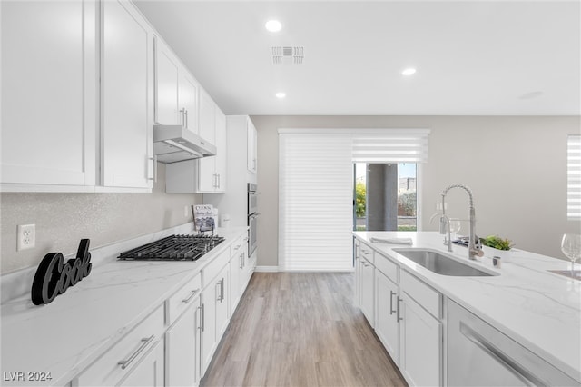 kitchen with white cabinets, sink, light stone countertops, light wood-type flooring, and stainless steel appliances