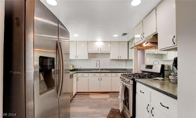 kitchen featuring under cabinet range hood, a sink, light wood-style floors, appliances with stainless steel finishes, and dark countertops