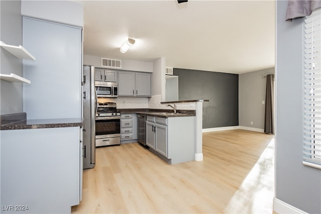 kitchen featuring appliances with stainless steel finishes, light wood-type flooring, kitchen peninsula, and gray cabinetry