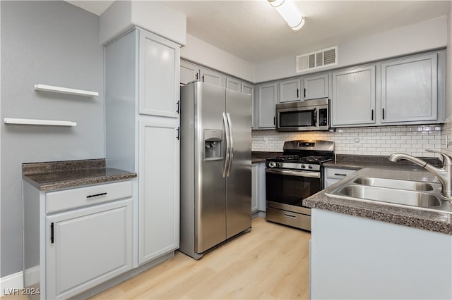 kitchen with light wood-type flooring, sink, decorative backsplash, stainless steel appliances, and gray cabinetry