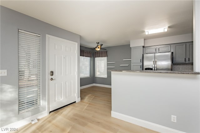 kitchen with light wood-type flooring, gray cabinetry, backsplash, stainless steel fridge with ice dispenser, and dark stone counters