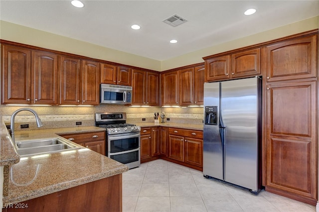 kitchen with light tile patterned flooring, tasteful backsplash, sink, stainless steel appliances, and light stone countertops