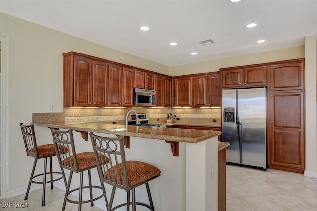 kitchen featuring light stone counters, kitchen peninsula, backsplash, appliances with stainless steel finishes, and a breakfast bar