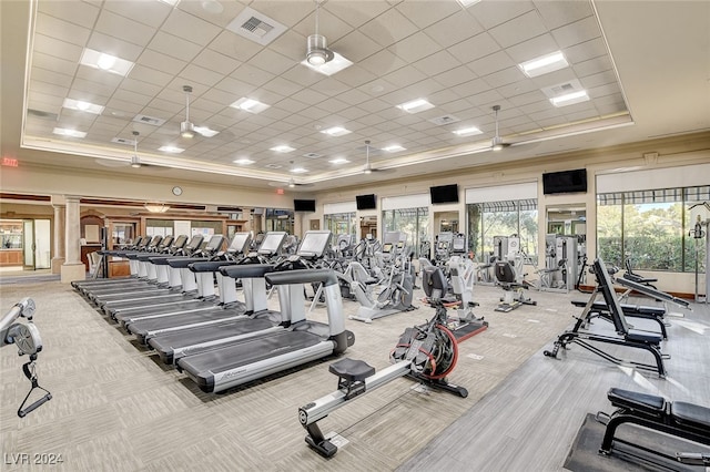 gym featuring decorative columns, light colored carpet, a paneled ceiling, a raised ceiling, and ceiling fan