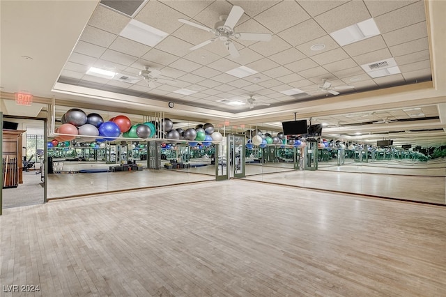 workout area featuring wood-type flooring, ceiling fan, a raised ceiling, and a paneled ceiling