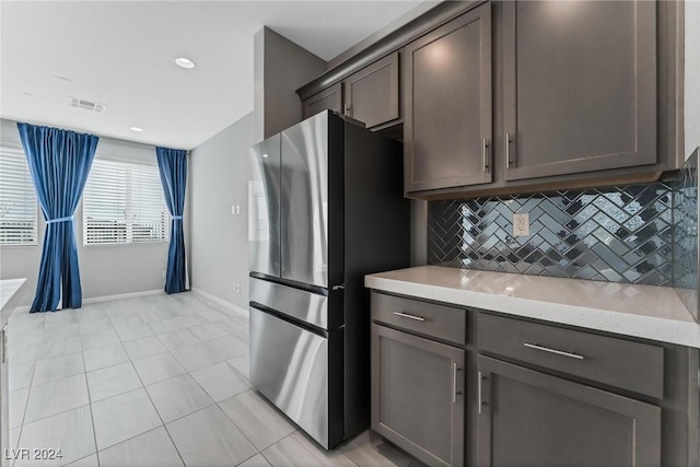 kitchen featuring stainless steel fridge, light tile patterned floors, tasteful backsplash, and light stone counters