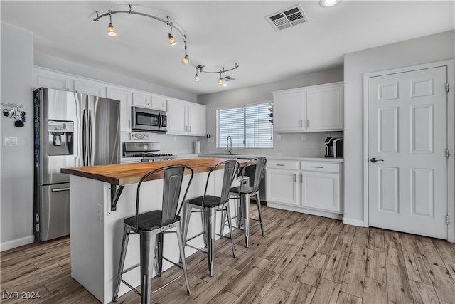 kitchen with a center island, a breakfast bar area, white cabinets, appliances with stainless steel finishes, and wooden counters