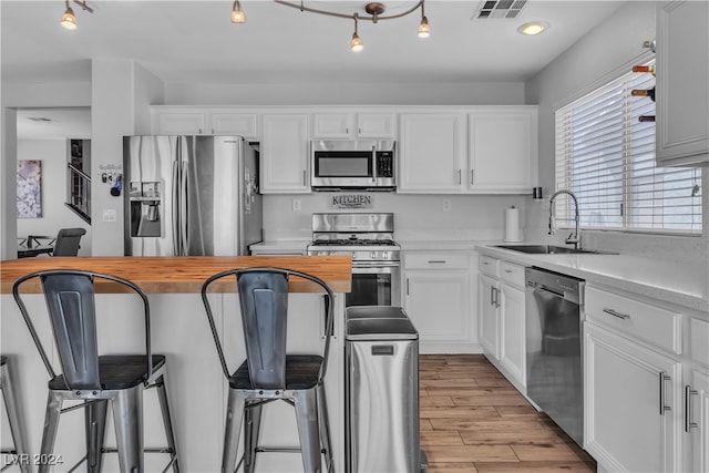 kitchen featuring light wood-type flooring, sink, white cabinets, a kitchen bar, and appliances with stainless steel finishes