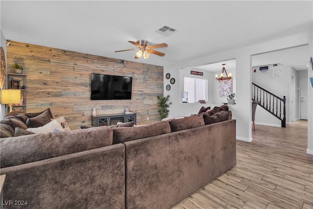 living room featuring ceiling fan with notable chandelier, light hardwood / wood-style flooring, a fireplace, and wood walls