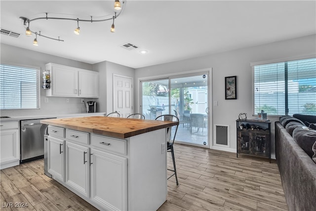 kitchen featuring white cabinets, a kitchen bar, a center island, stainless steel dishwasher, and wood counters