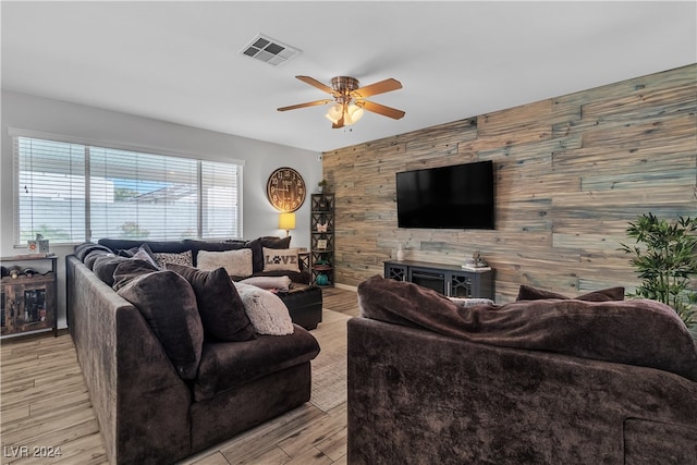 living room featuring light wood-type flooring, wooden walls, and ceiling fan