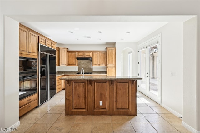 kitchen featuring a kitchen bar, black appliances, a kitchen island with sink, and light stone counters