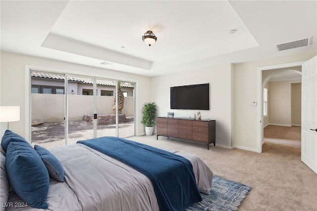 bedroom with light carpet, access to exterior, and a tray ceiling