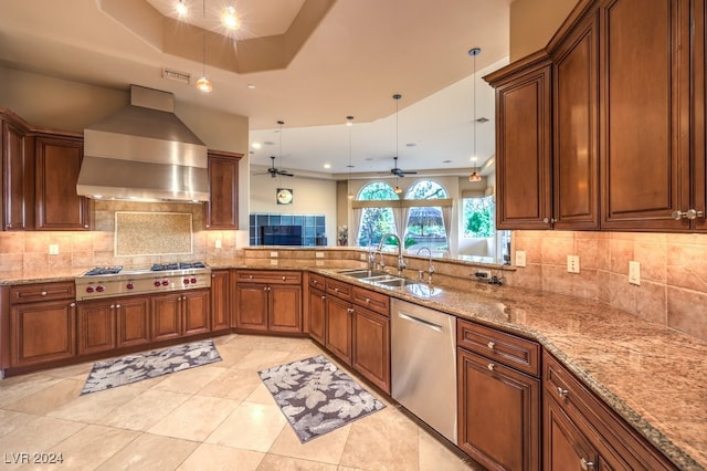 kitchen featuring appliances with stainless steel finishes, sink, pendant lighting, wall chimney exhaust hood, and a tray ceiling