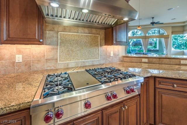 kitchen with wall chimney exhaust hood, decorative backsplash, hanging light fixtures, ceiling fan, and stainless steel gas stovetop