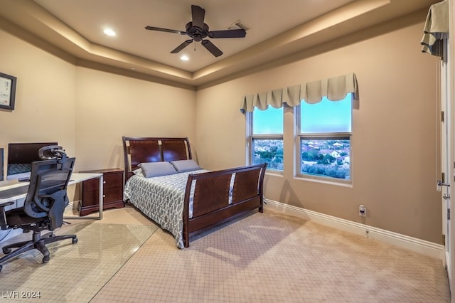 carpeted bedroom with ceiling fan and a tray ceiling