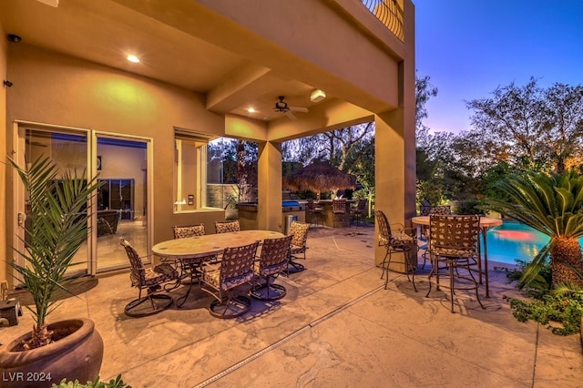 patio terrace at dusk featuring ceiling fan and area for grilling